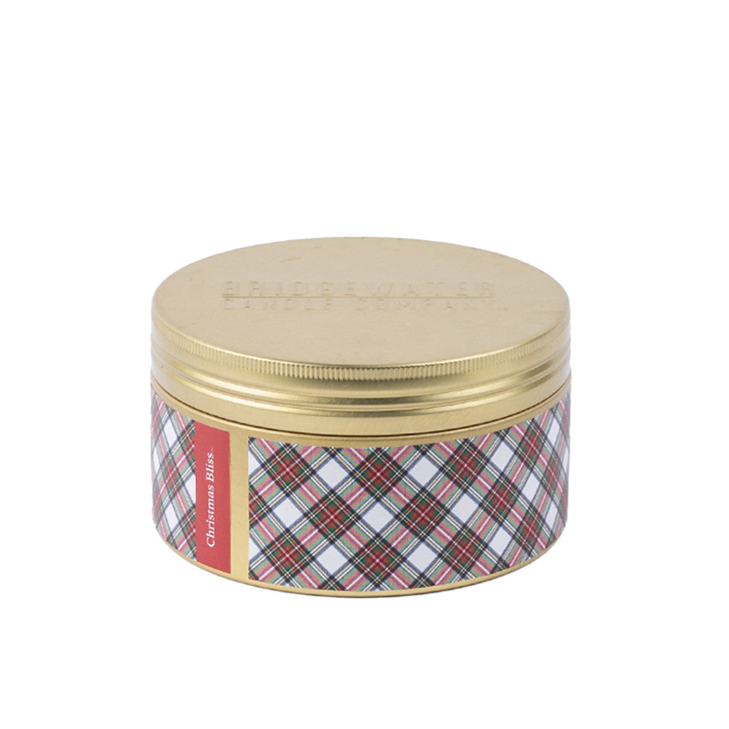 The Bridgewater Candle Company Christmas Bliss Holiday 3-Wick Tin Candle features a gold lid and plaid label with a red "Christmas Bliss" stripe. It's displayed on a white background.