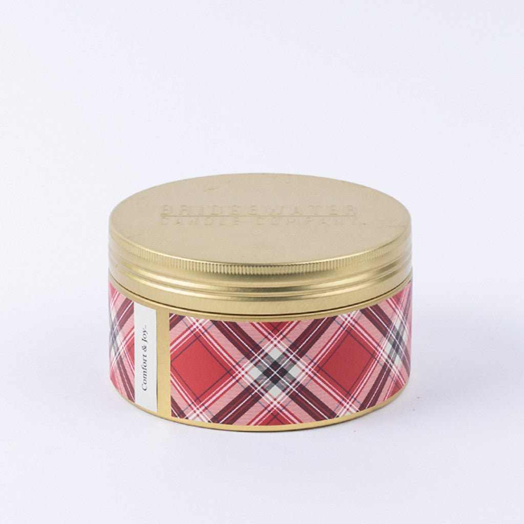 The Bridgewater Candle Company Comfort & Joy Holiday 3-Wick Tin Candle features a gold lid, red plaid label, and soy-blend wax. With up to 45 hours of burn time, it fills your space with the festive Comfort & Joy fragrance.