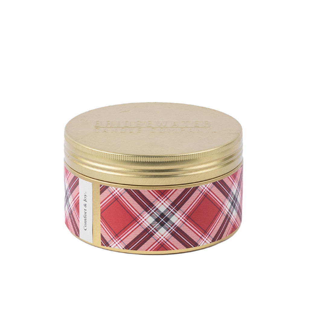 The Comfort & Joy Holiday 3-Wick Tin Candle by Bridgewater Candle Company features a gold lid, red plaid design, and "Cranberry & Bay" label. Made with soy-blend wax for a festive fragrance.