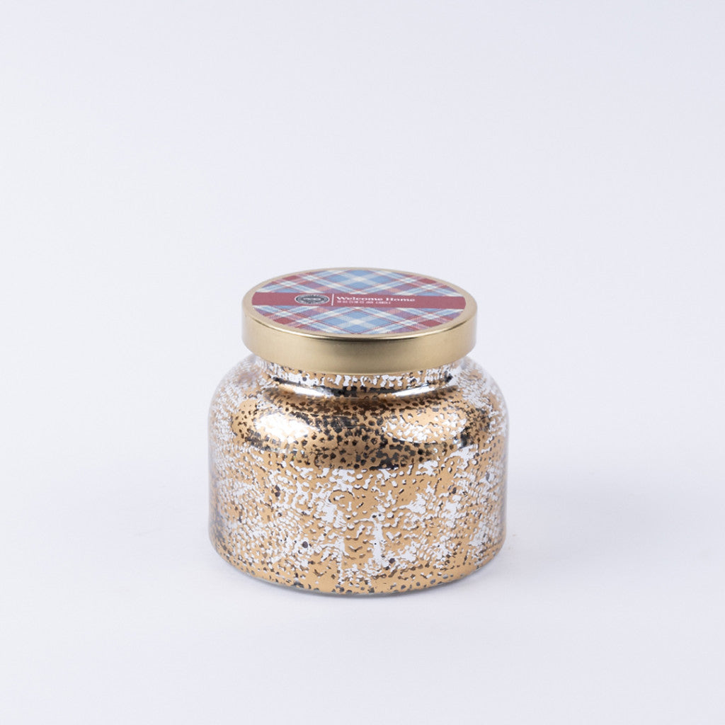 The Welcome Home Mercury Jar Candle by Bridgewater Candle Company features a gold and white speckled glass jar with a plaid-accented gold lid. This soy-blend candle brings premium home fragrance to any space.