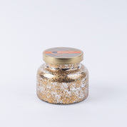 A Harvest Pumpkin Mercury Jar Candle by Bridgewater Candle Company, featuring a clear glass jar with a gold metallic lid and filled with gold and white speckled decorative material, set against a plain white background.