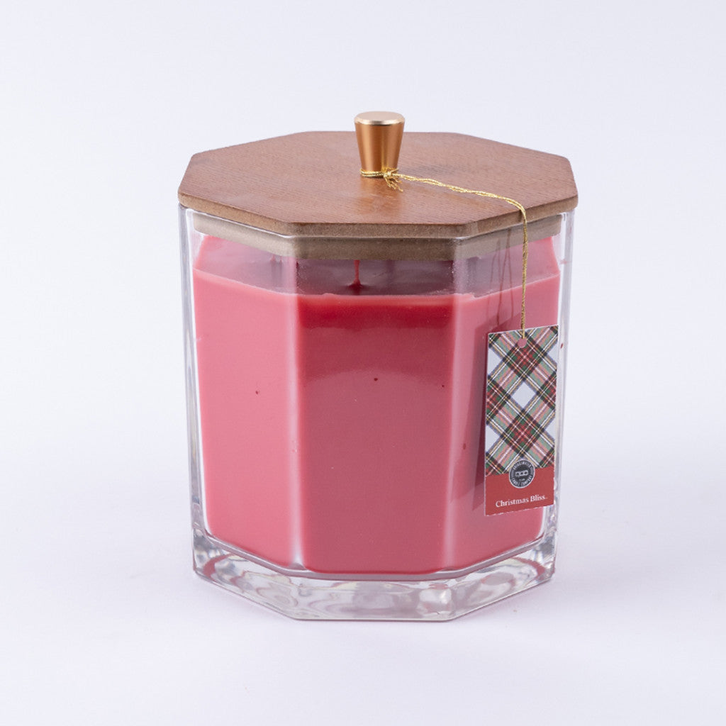 The Christmas Bliss Holiday Large Decorative Candle by Bridgewater Candle Company features pink soy-blend wax in a clear hexagonal jar with wooden lid, gold knob, and a festive plaid tag.