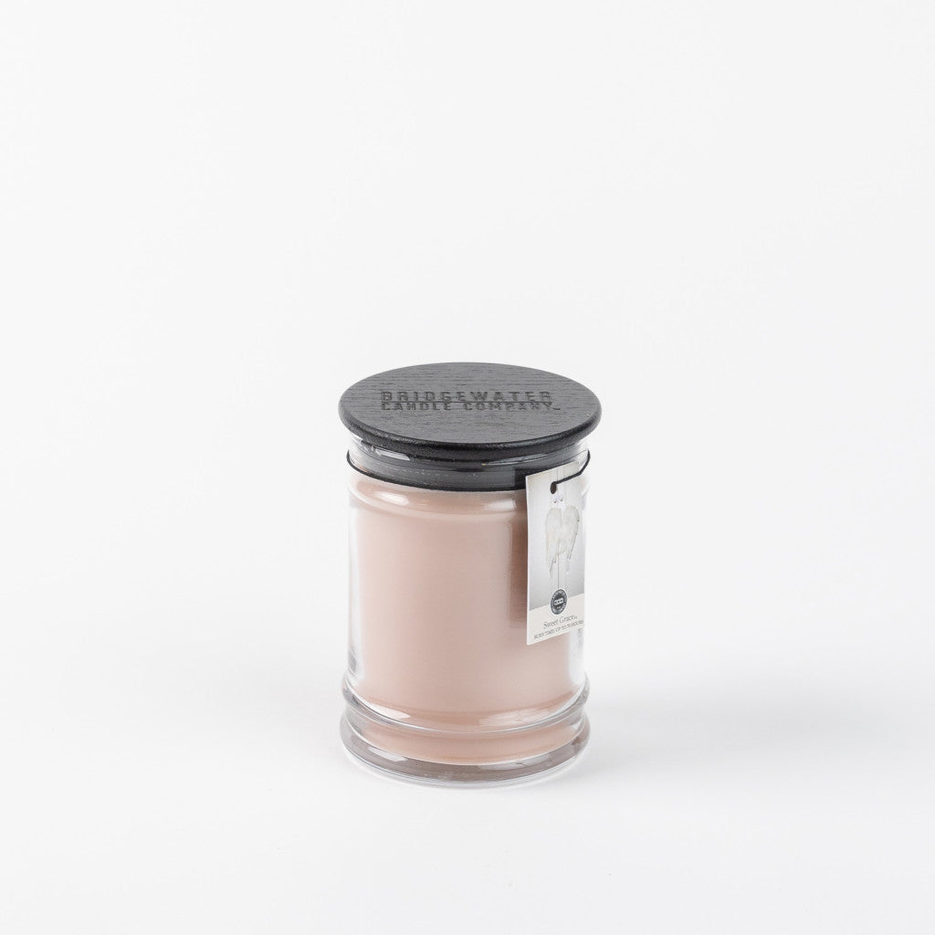 The Sweet Grace 8oz Jar Candle by Bridgewater Candle Company has light pink wax in a glass jar with a black lid and side tag. Its lively, passionate fruit scent stands out beautifully against a simple white background.