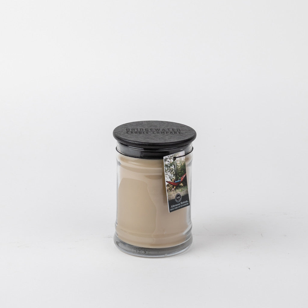 The Bridgewater Candle Company Afternoon Retreat 8oz Jar Candle features beige wax in a glass jar with a black lid and a tag, creating a cozy touch against its white background.