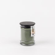 A green Festive Frasier 8oz Jar Candle by Bridgewater Candle Company in a clear glass jar with a black lid. A small tag featuring a tree illustration and Festive Frasier text adds charm, set against a plain white background.