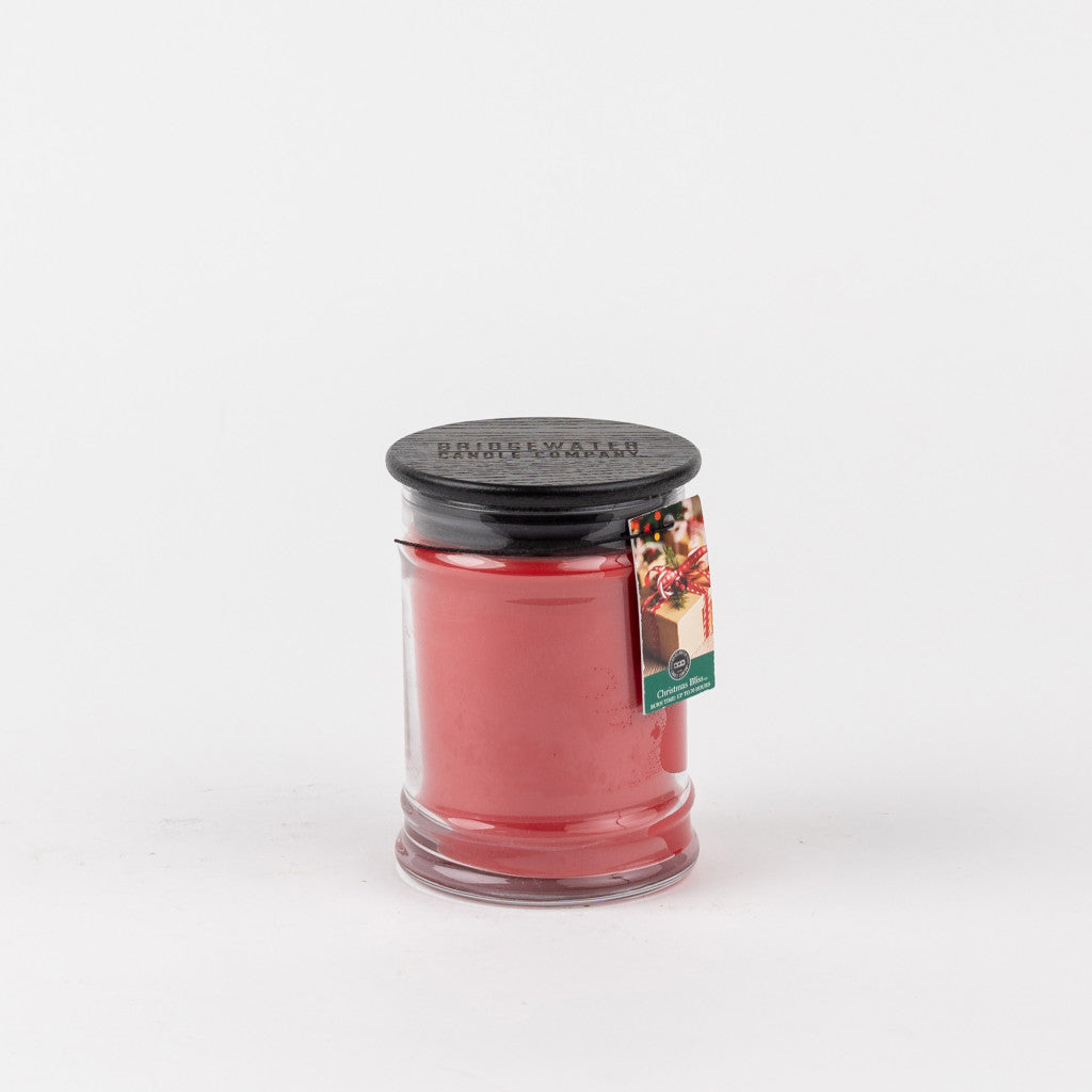 The Bridgewater Candle Company Christmas Bliss 8oz Holiday Jar Candle features a red jar, black lid, and festive tag, showcasing its signature scent against a plain white background.