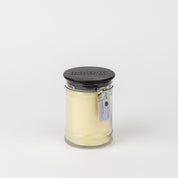 A Bridgewater Candle Company Laundry Line 8oz Jar Candle with creamy white wax and a black lid sits on a plain white background, featuring a scent label and image attached to the jar’s neck.