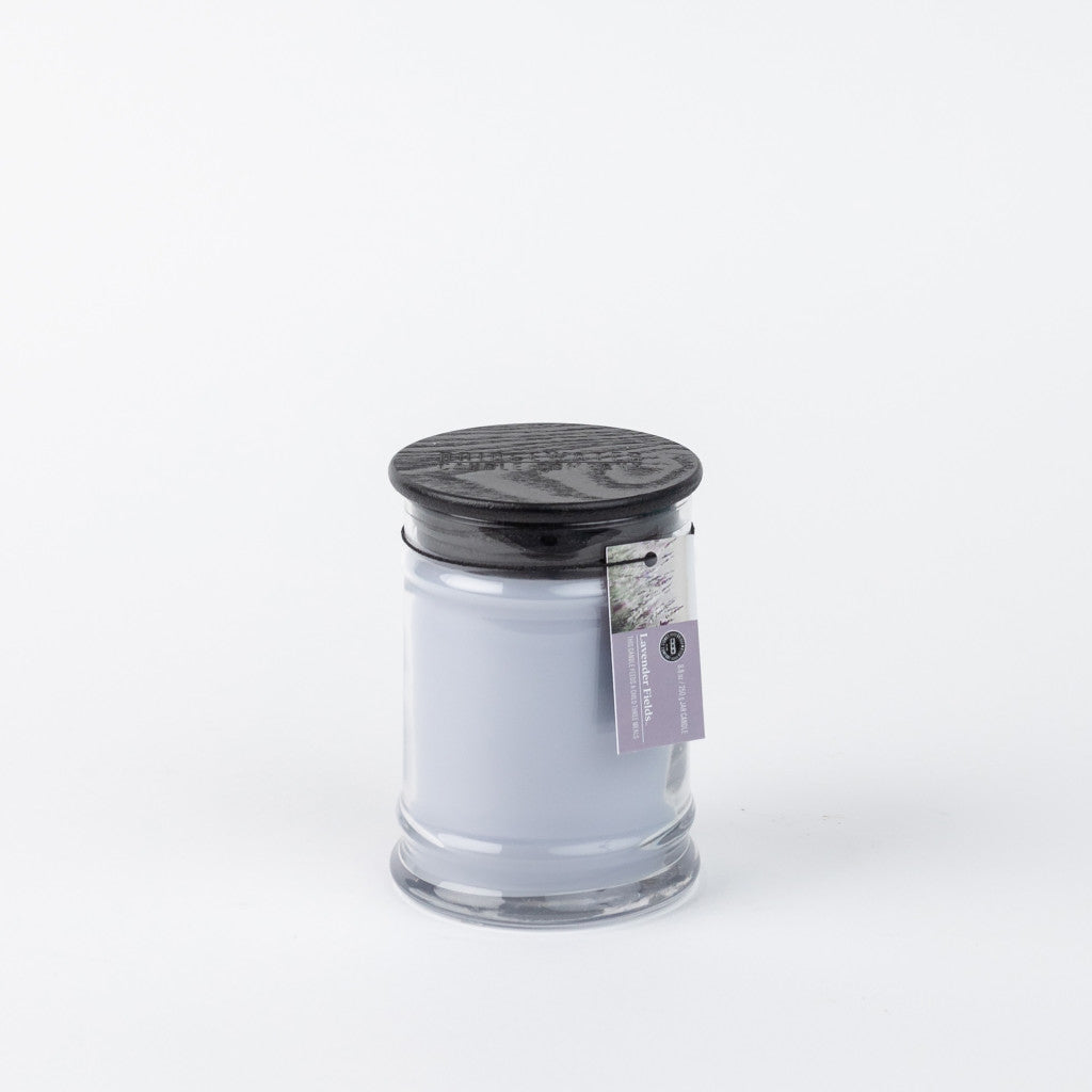 The Bridgewater Candle Company Lavender Fields 8oz Small Jar Candle features pale lavender wax in a glass jar with a black textured lid and lavender tag, filling your space with the serene scent of lavender fields.