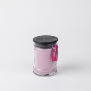 The Bridgewater Candle Company XOXO 8oz Small Jar Candle features light pink soy-blend wax, a black wooden lid, and a pink tag on top, all set against a plain white background.