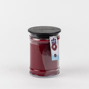 The Bridgewater Candle Company Welcome Home 18oz Large Jar Candle features a black lid, comes in a clear glass jar with a wreath tag, and hints at its inviting fragrance, all set against a plain white background.