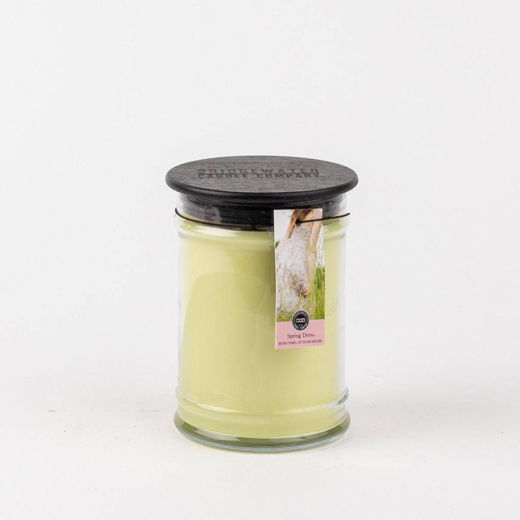 The Spring Dress 18oz Large Jar Candle by Bridgewater Candle Company features pale yellow wax, a black lid, and a label with a white duck and pink text. This floral candle stands out against a plain white background.