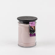 A Kiss in the Rain 18oz Large Jar Candle by Bridgewater Candle Company sits in a clear glass jar with black lid, accented by a purple tag. The pink candle is infused with Bridgewater fragrance and displayed against a plain white background.