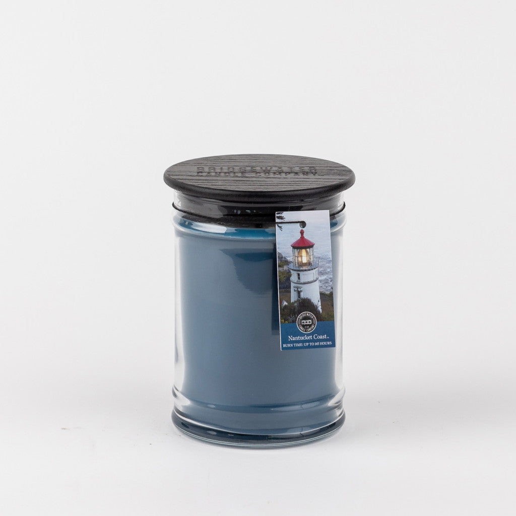 The Nantucket Coast 18oz Large Jar Candle by Bridgewater Candle Company features a blue wax in a clear glass jar with a black lid and lighthouse label. The photo shows the candle on a plain white background.