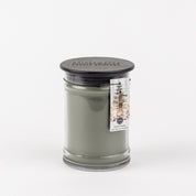 The Bridgewater Candle Company Festive Frasier 18oz Large Jar Candle features grayish-green wax, a black lid, and a pine tree label for a fresh, festive touch. Perfect for holiday ambiance. Shown on a plain white background.