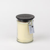 The Bridgewater Candle Company Laundry Line 18oz Large Jar Candle features white soy-blend wax in a large jar with a black lid. A small label with text and a plant image adorns the jar, set against a plain white background for fresh fragrance appeal.