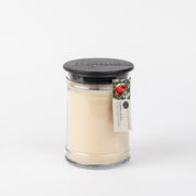 The Bridgewater Candle Company Comfort & Joy 18oz Large Jar Candle features creamy white wax, a black lid topped with a tag showing a red bird and green leaves, all set against a plain white background.