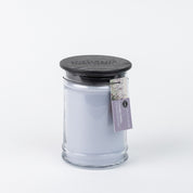 The Bridgewater Candle Company Lavender Fields 18oz Large Jar Candle features light lavender wax, a black wooden lid, and a tag with the fragrance name and a lavender flower image. The background is plain white.