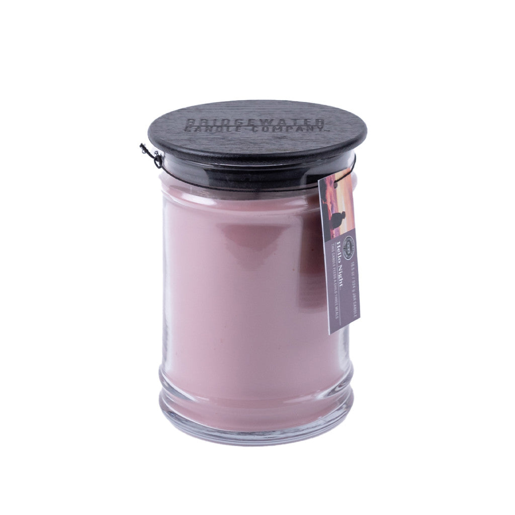 The Bridgewater Candle Company Hello Night 18oz Jar Candle features pink soy-blend wax in a clear glass jar with a black lid and hanging product tag, set against a white background.