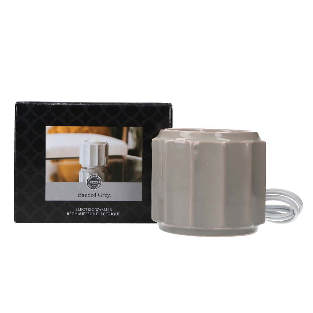 The Wax Warmer-Grey Banded by Bridgewater Candle Company is shown with its black box featuring a photo and product name. The coiled white cord sits beside it, making it ideal for use with wax melts or home fragrance oils.
