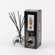 A Bridgewater Candle Company Festive Frasier Reed Diffuser with black fiber reeds stands by its box, which features a person in a snowy forest and describes the Festive Frasier fragrance.