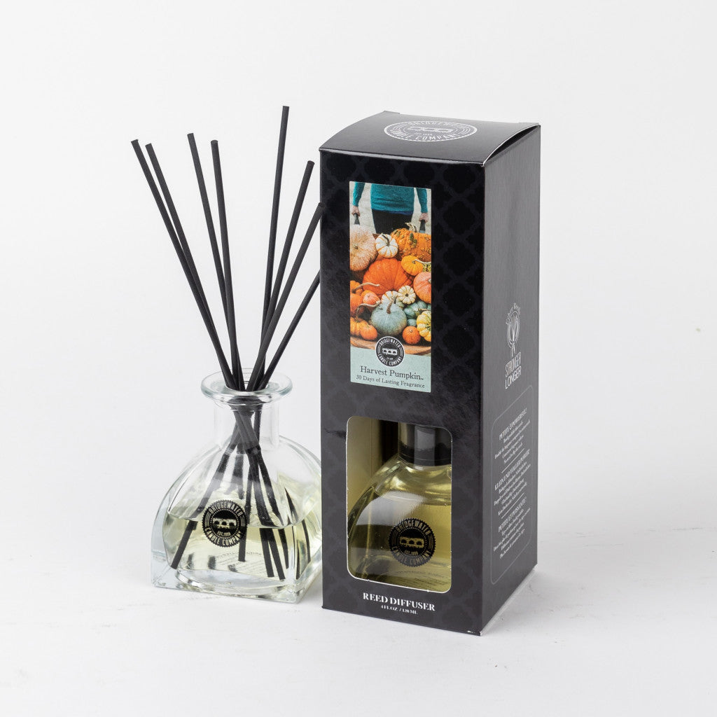 The Bridgewater Candle Company Harvest Pumpkin Reed Diffuser features a clear glass bottle with black reeds and a light-colored liquid beside its pumpkin-themed box—perfect for adding a cozy autumn fragrance to your home.