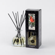 The Bridgewater Candle Company Comfort & Joy Reed Diffuser with black fiber reeds is shown beside its black box, which features a red cardinal and the product label, all set against a plain white background.
