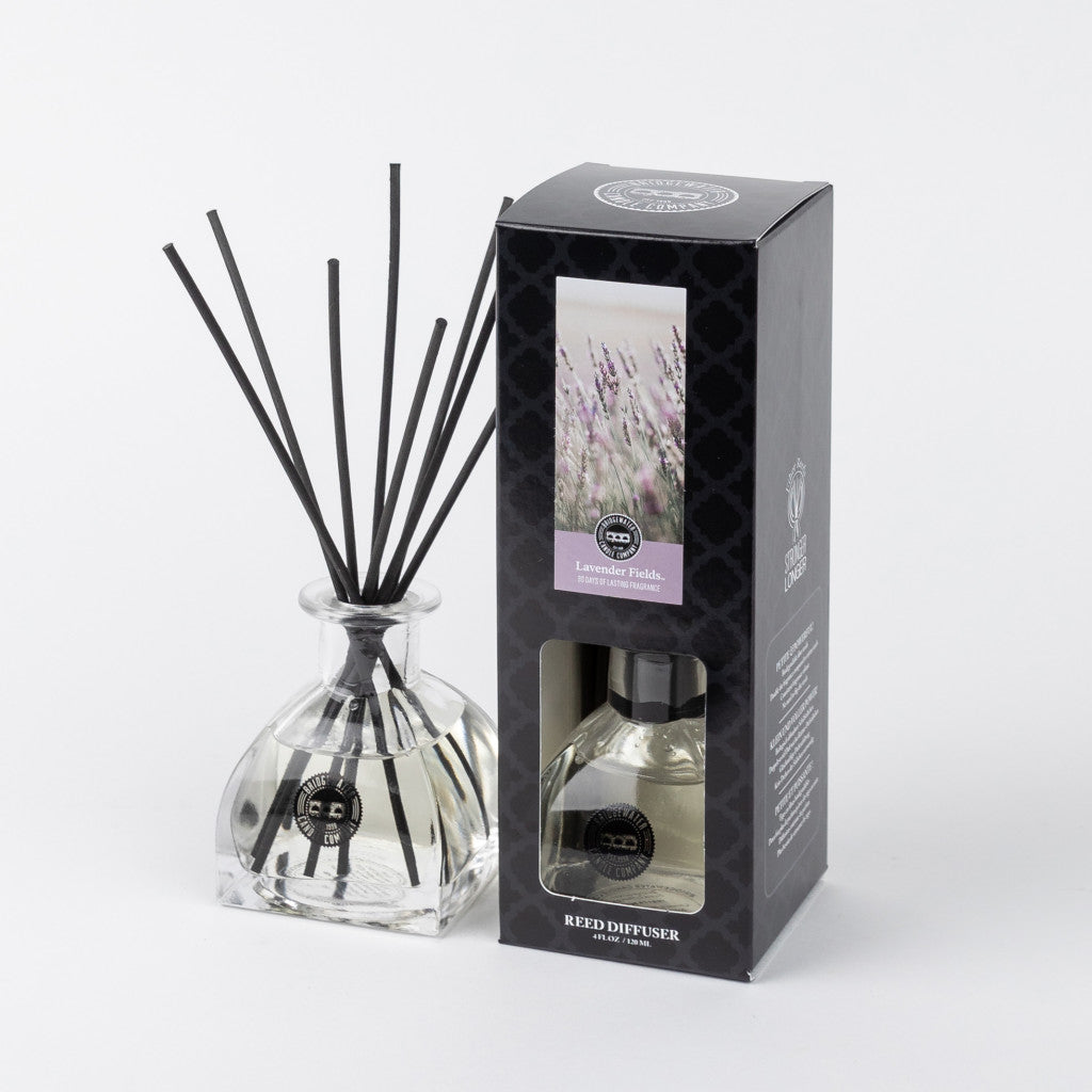 The Bridgewater Candle Company Lavender Fields Reed Diffuser, with fiber reeds and clear liquid, is displayed beside its black box packaging featuring lavender flower imagery and the “Lavender Fields” label.