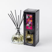 The XOXO Reed Diffuser by Bridgewater Candle Company features a glass bottle with black fiber reeds, paired with sleek black packaging adorned with colorful flowers and a window showcasing the premium fragrance inside.