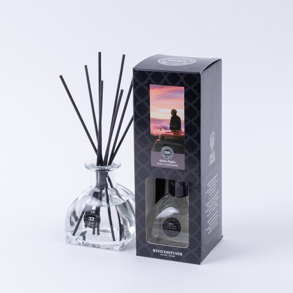 The Bridgewater Candle Company Hello Night Reed Diffuser features fiber reeds in a glass bottle beside its elegant black box with a sunset image—ideal for elevating your space with premium fragrance.