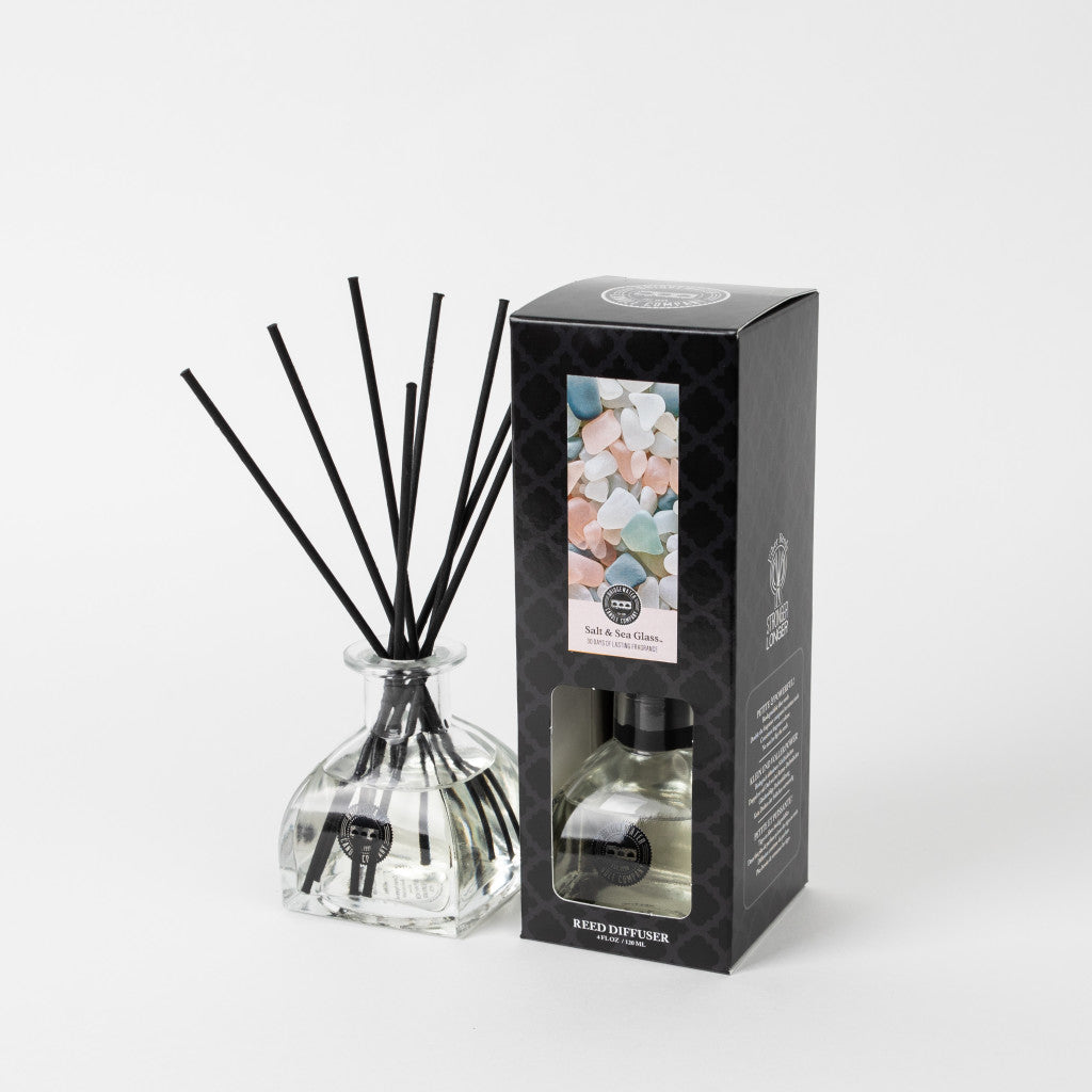 The Bridgewater Candle Company Salt & Sea Glass Reed Diffuser sits beside its modern black box, decorated with colorful salt crystals, creating an elegant home fragrance display against a clean white background.