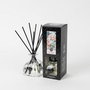 The Bridgewater Candle Company Salt & Sea Glass Reed Diffuser sits beside its modern black box, decorated with colorful salt crystals, creating an elegant home fragrance display against a clean white background.