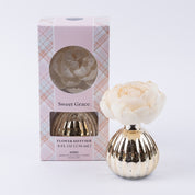 The Bridgewater Candle Company Sweet Grace Mercury Flower Diffuser features an ivory faux flower in a gold ribbed vase, paired with pink plaid packaging with a circular window—an elegant addition to your home fragrance décor.