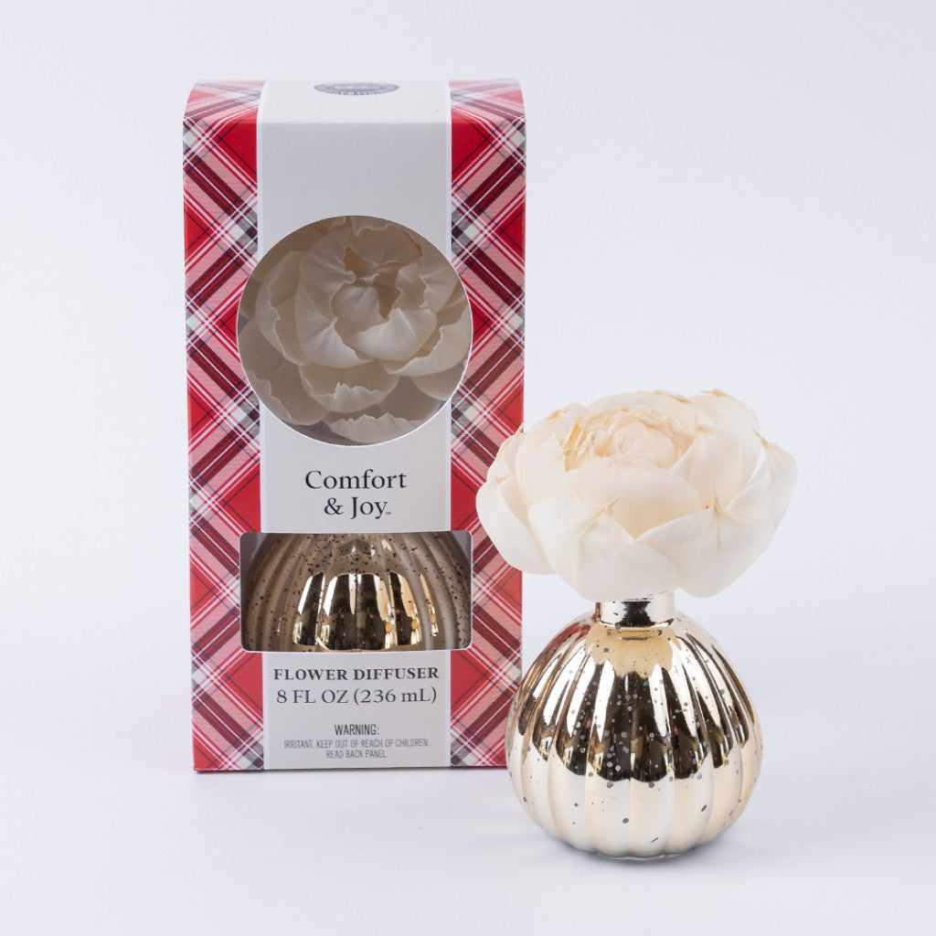 The Bridgewater Candle Company’s Comfort & Joy Holiday Mercury Flower Diffuser features a gold-ribbed design and cream bloom, displayed in its red plaid box with a clear window that showcases the diffuser and flower inside.