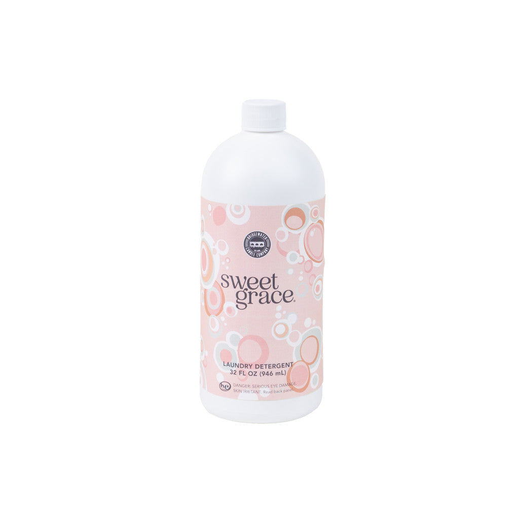 A white plastic bottle of Bridgewater Candle Companys Sweet Grace 32oz Laundry Detergent features a pink label with bubble designs, offering a luxurious formula and long-lasting scent.