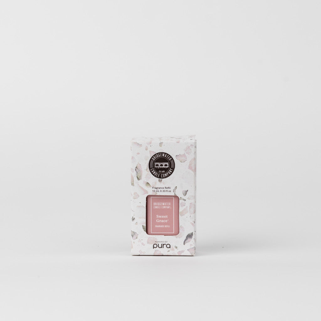 A white rectangular box of Bridgewater Candle Company’s Pura + Bridgewater Fragrance Refill in Sweet Grace stands against a plain background, showcasing a pink and gray pattern with black and pink labels; compatible with Pura Smart Vials.