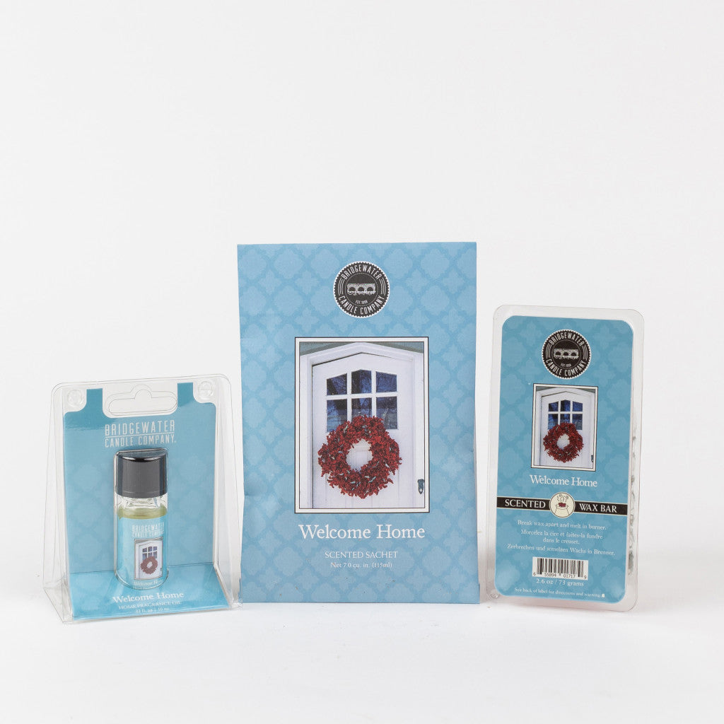 The Bridgewater Candle Company Welcome Home Flameless Bundle features a scented sachet, fragrance oil, and wax bar in matching blue packaging with a door wreath design, all displayed against a white background.
