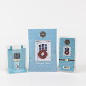 The Bridgewater Candle Company Welcome Home Flameless Bundle features a scented sachet, fragrance oil, and wax bar in matching blue packaging with a door wreath design, all displayed against a white background.