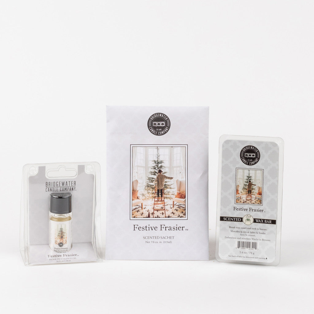 The Festive Frasier Flameless Bundle from Bridgewater Candle Company includes a home fragrance oil, sachet, and soy-blend wax bar—all in winter holiday packaging with a decorated Christmas tree.