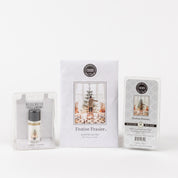 The Festive Frasier Flameless Bundle from Bridgewater Candle Company includes a home fragrance oil, sachet, and soy-blend wax bar—all in winter holiday packaging with a decorated Christmas tree.