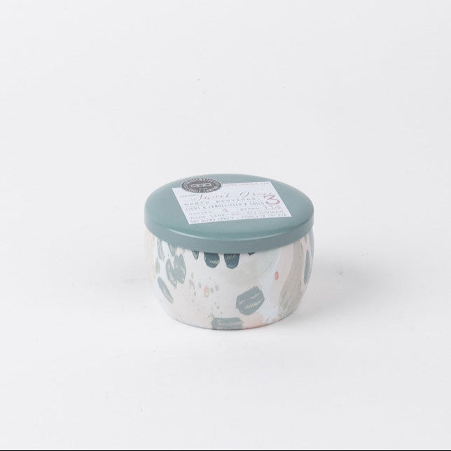 The Sweet Grace Collection Candle #033 by Bridgewater Candle Company is a small, round ceramic candle with a teal lid, pastel abstract patterns, and soy-blend wax, shown on a plain white background.