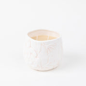 The Sweet Grace Collection Candle #057 by Bridgewater Candle Company features a white ceramic holder with a floral motif, filled with cream-colored soy-blend wax and two wicks—an elegant luxury fragrance accent for your home.