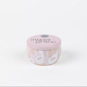 The Bridgewater Candle Company Sweet Grace Collection Candle #059 is a small, round, pale pink travel-sized soy-blend candle with a lid and a white and beige floral patterned jar. Set against a white background for a clean look.