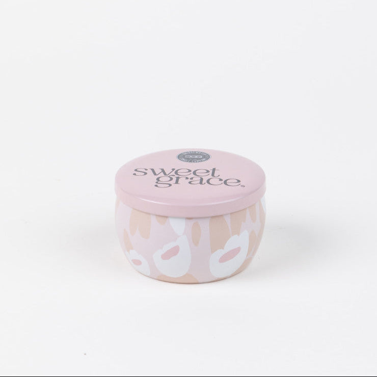The Bridgewater Candle Company Sweet Grace Collection Candle #059 is a small, round, pale pink travel-sized soy-blend candle with a lid and a white and beige floral patterned jar. Set against a white background for a clean look.