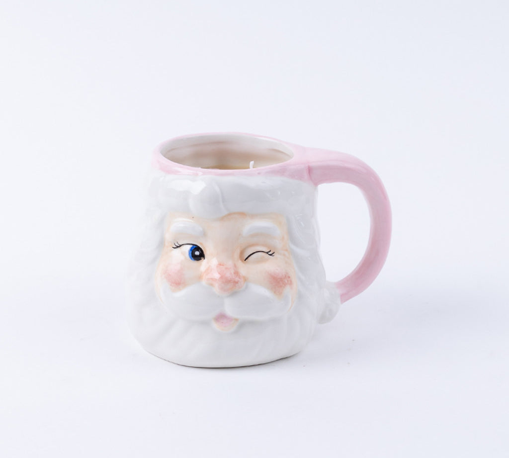 The Bridgewater Candle Company Sweet Grace Santa Mug is a ceramic reusable mug shaped like a winking Santa with a white beard, rosy cheeks, and a pink handle—ideal for holiday candle lovers or as festive decor.