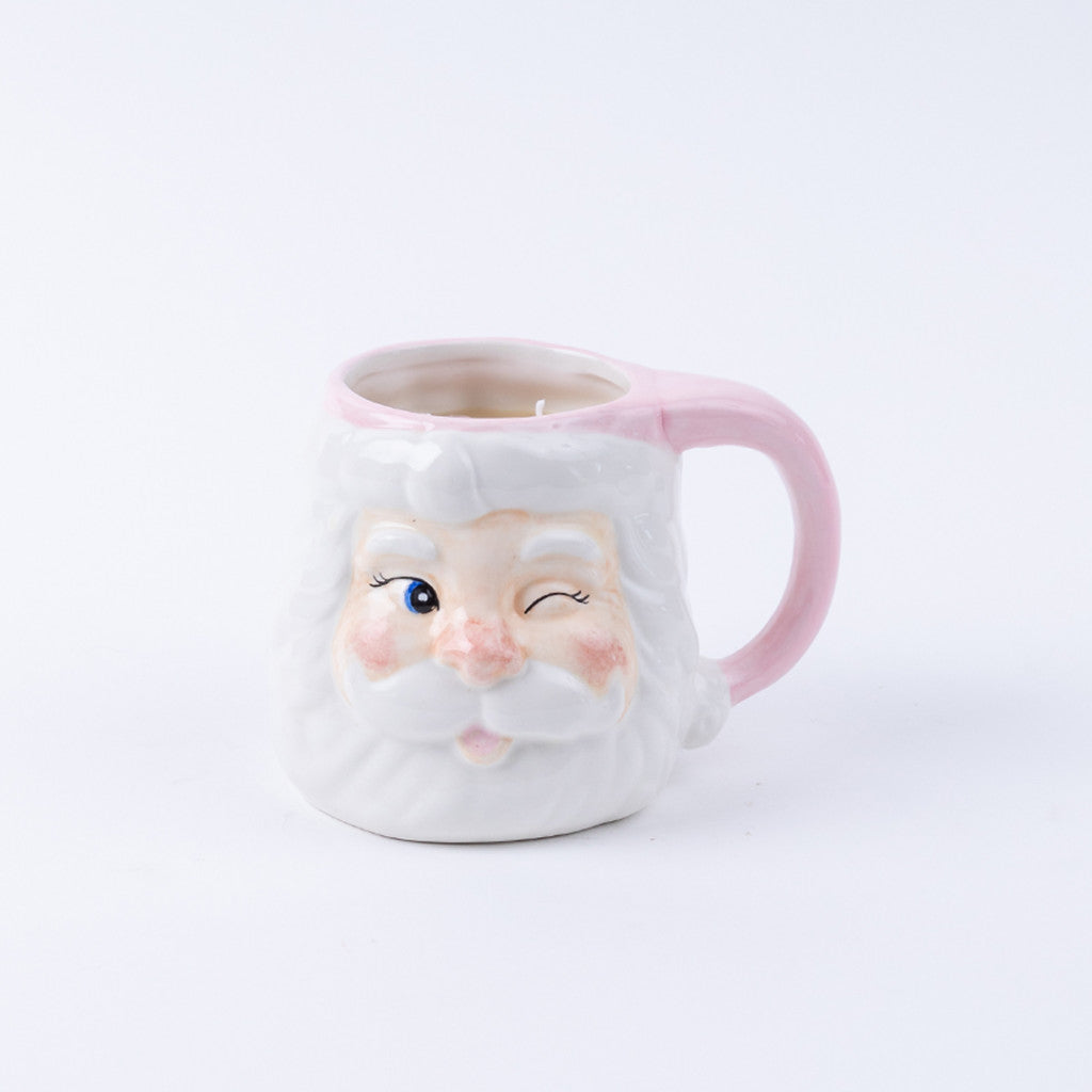 The Bridgewater Candle Company Sweet Grace Santa Mug is a ceramic reusable mug shaped like a winking Santa with a white beard, rosy cheeks, and a pink handle—ideal for holiday candle lovers or as festive decor.