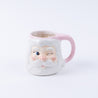 The Bridgewater Candle Company Sweet Grace Santa Mug is a ceramic reusable mug shaped like a winking Santa with a white beard, rosy cheeks, and a pink handle—ideal for holiday candle lovers or as festive decor.