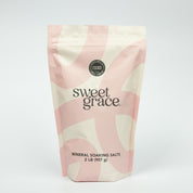 A pink and cream resealable pouch labeled “Sweet Grace Soaking Salts” by Bridgewater Candle contains a blend of Epsom and Pink Himalayan Sea Salt, with a circular seal and 2 lb (907 g) weight displayed on a plain white background.