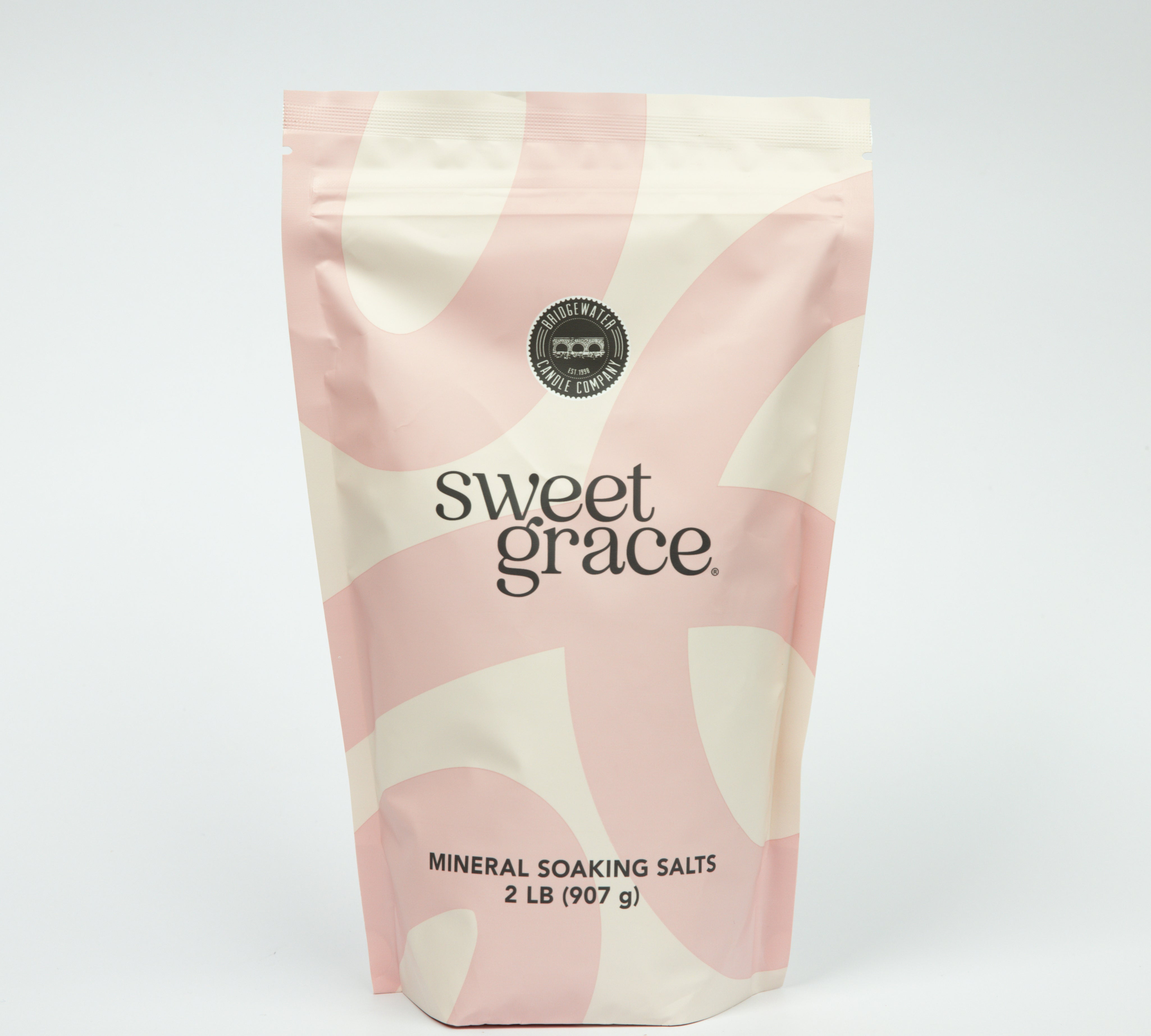 A pink and cream resealable pouch labeled “Sweet Grace Soaking Salts” by Bridgewater Candle contains a blend of Epsom and Pink Himalayan Sea Salt, with a circular seal and 2 lb (907 g) weight displayed on a plain white background.