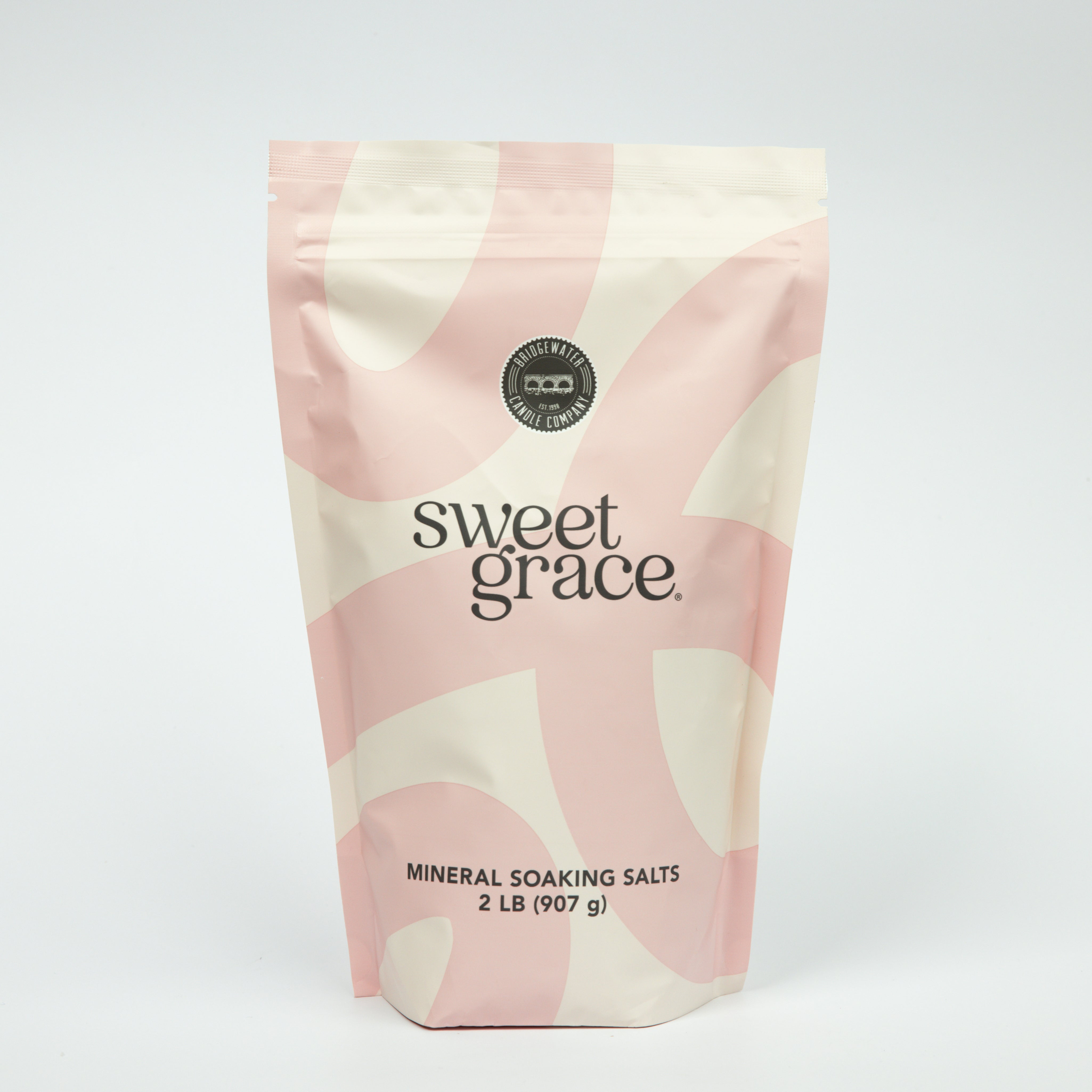 A pink and cream resealable pouch labeled “Sweet Grace Soaking Salts” by Bridgewater Candle contains a blend of Epsom and Pink Himalayan Sea Salt, with a circular seal and 2 lb (907 g) weight displayed on a plain white background.