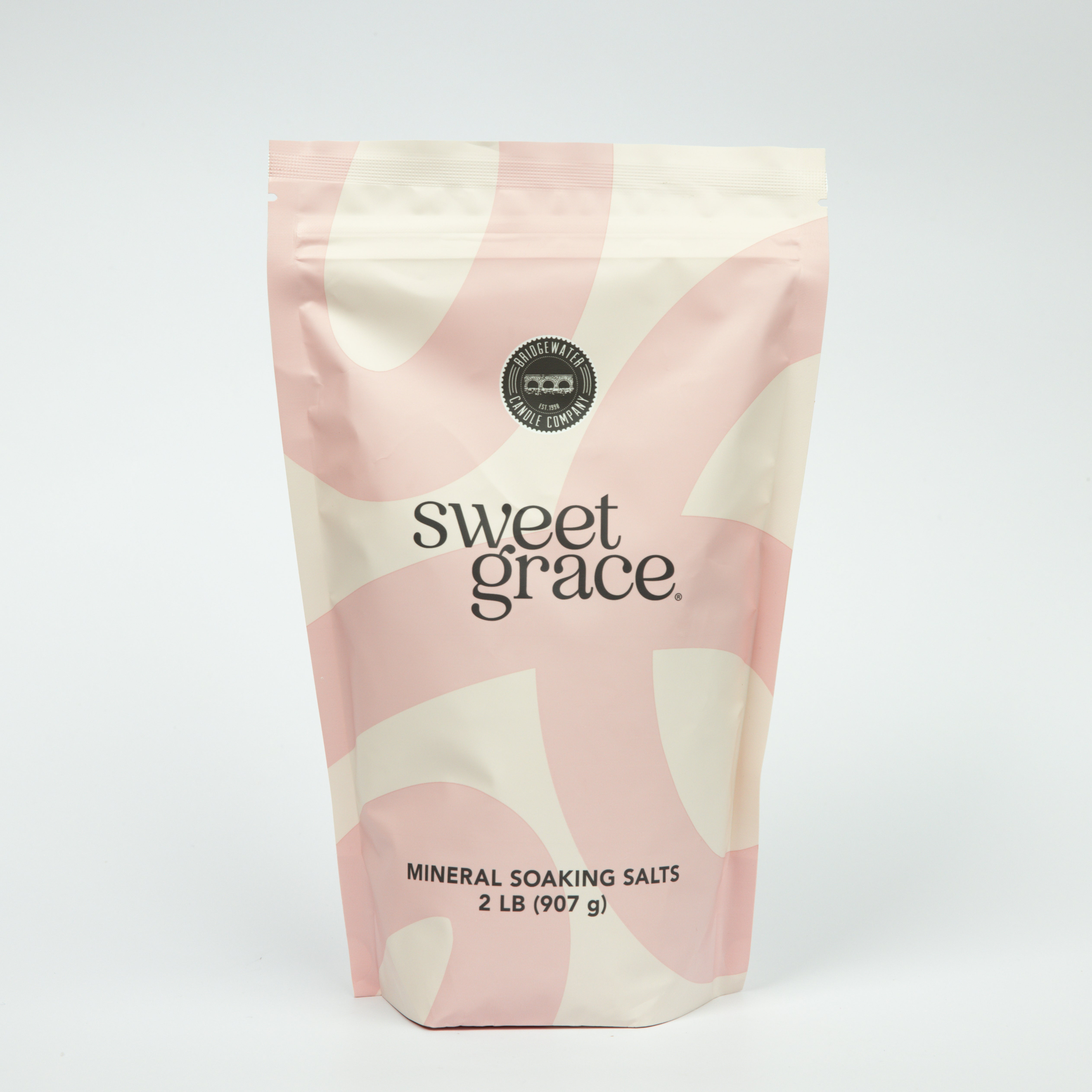 A pink and cream resealable pouch labeled “Sweet Grace Soaking Salts” by Bridgewater Candle contains a blend of Epsom and Pink Himalayan Sea Salt, with a circular seal and 2 lb (907 g) weight displayed on a plain white background.
